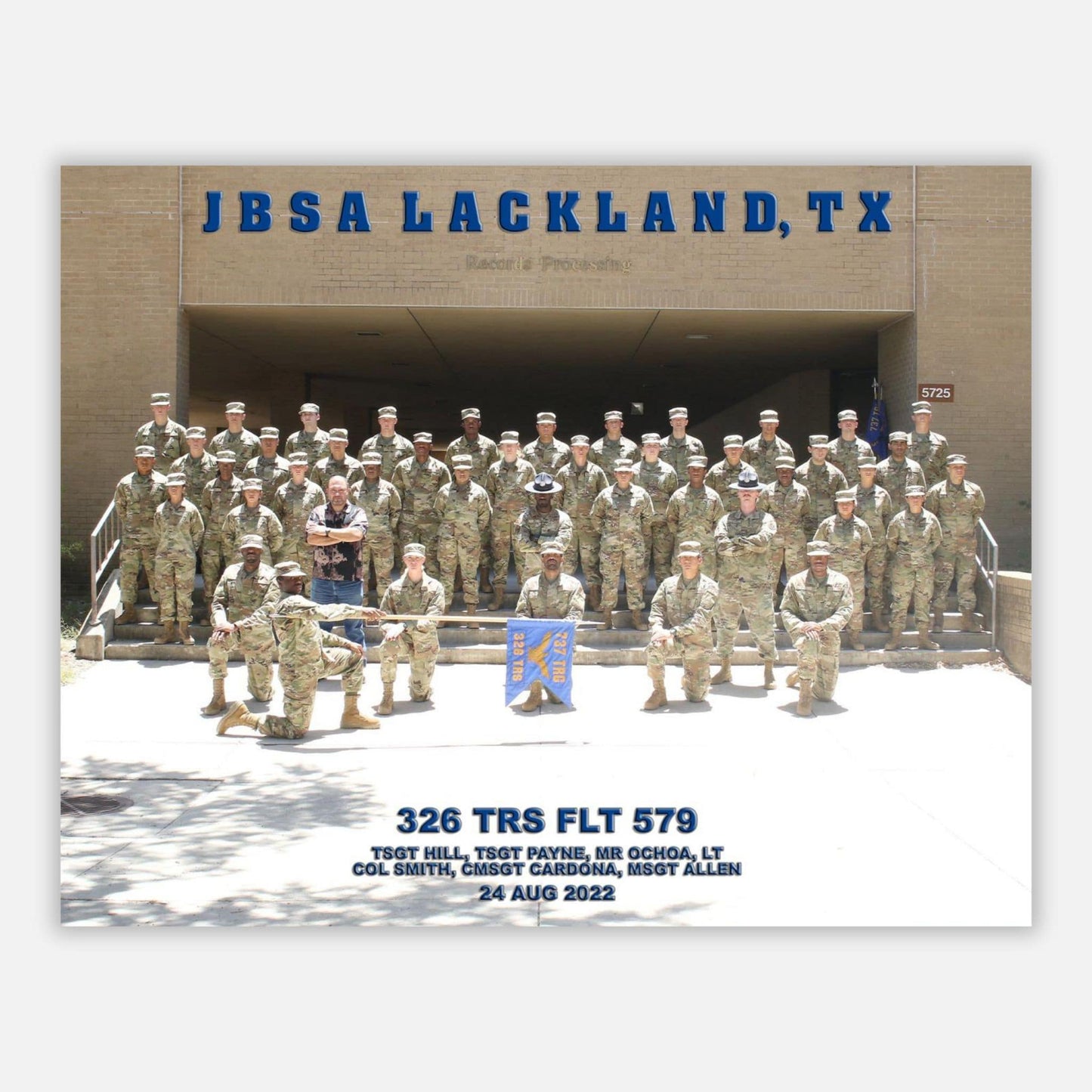 A group photograph of U.S. Air Force personnel at JBSA Lackland, TX, in a formation in front of a building entrance.