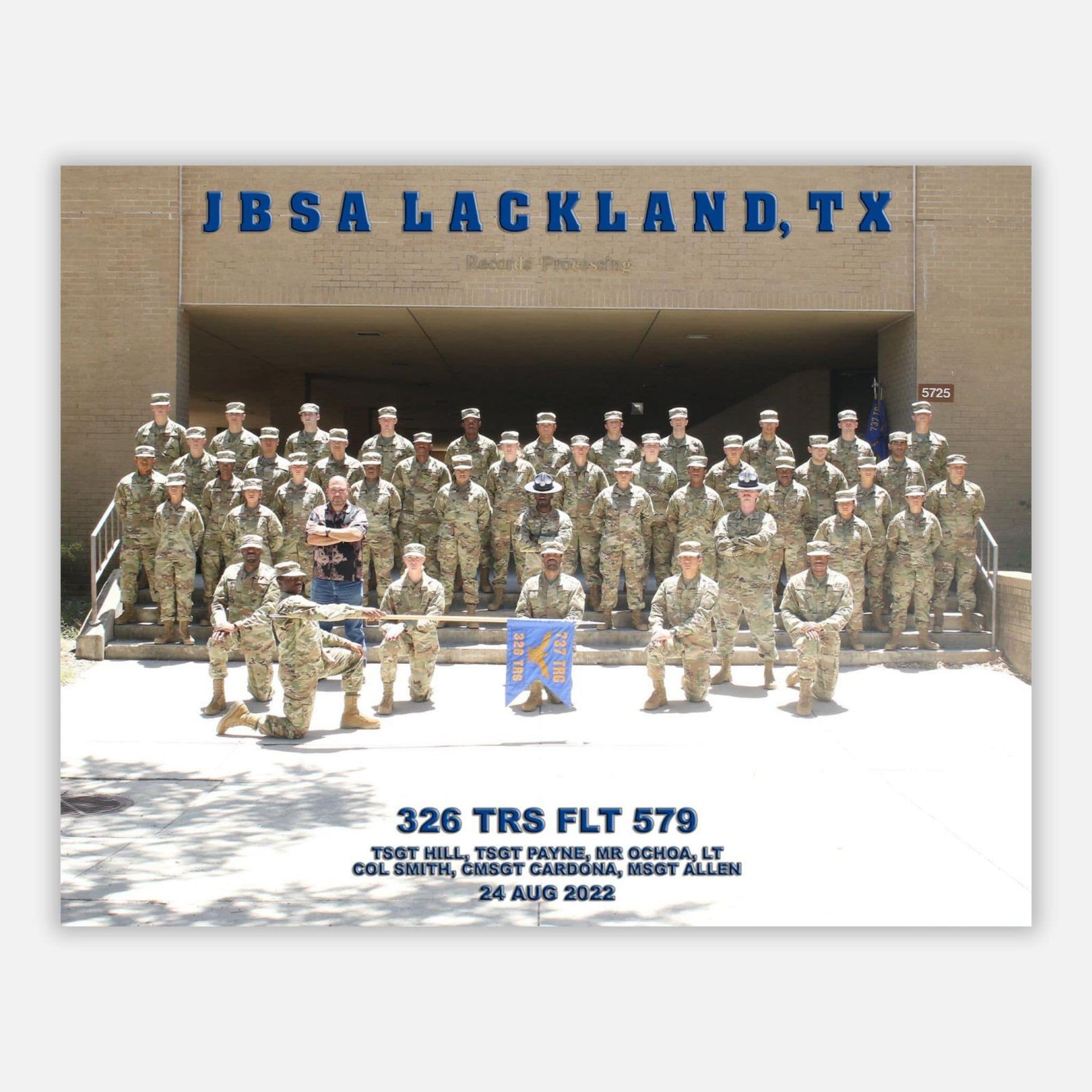A group photograph of U.S. Air Force personnel at JBSA Lackland, TX, in a formation in front of a building entrance.